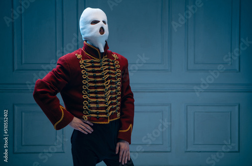 Young man, medieval hussar wearing white colors balaclava on dark blue background. Concept of comparison of eras, art, history. Creative collage. photo