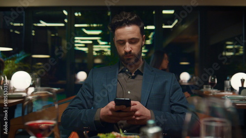 Focused businessman sitting restaurant. Respectable man texting mobile phone.