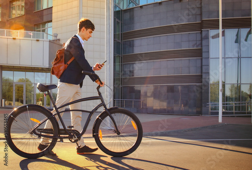 Young businessman with bicycle and smartphone on city street