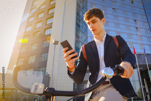 Young businessman with bicycle and smartphone on city street photo