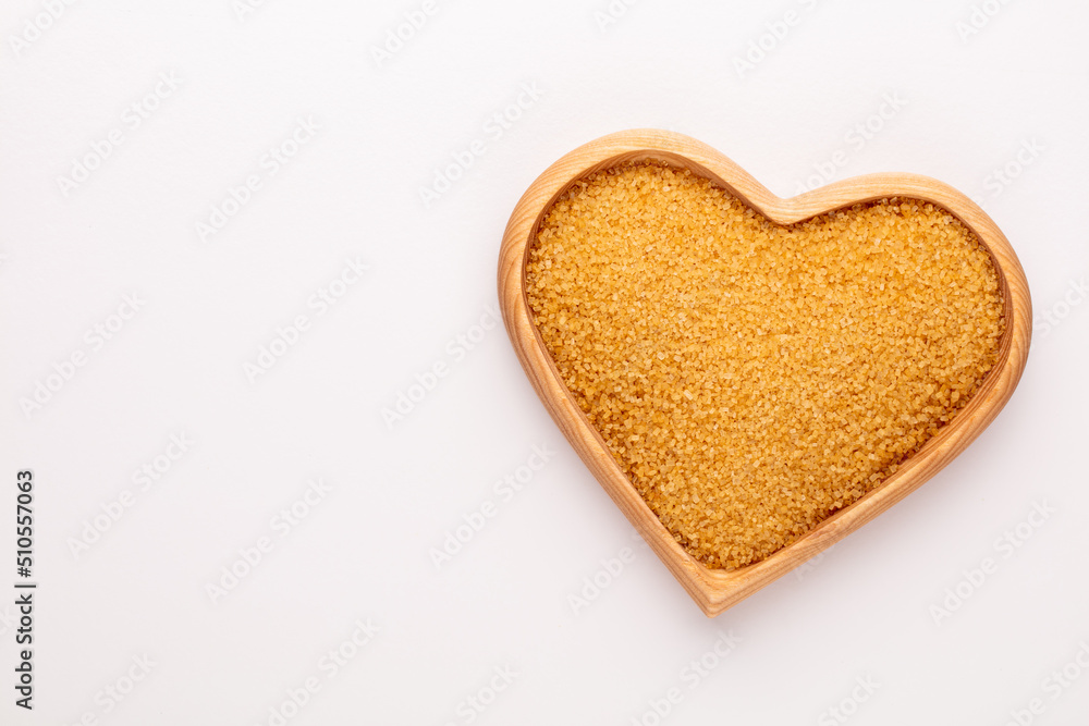 Brown sugar in heart wooden bowl shape on pasttel background. Brown sugar in heart wooden bowl shape on pasttel background.