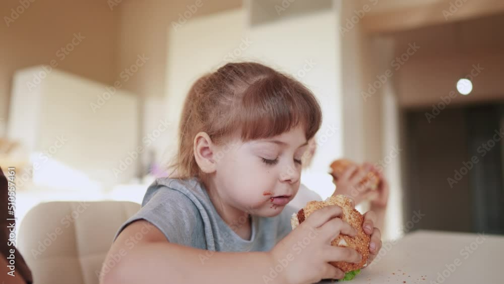 children eat burgers. fast food burger. a group of small children in the kitchen greedily fun eat fast food burgers. big family small kids having breakfast in the morning in the kitchen eating burger children eat burgers. fast food burger. a group of small children in the kitchen greedily fun eat fast food burgers. big family small kids having breakfast in the morning in the kitchen eating burger