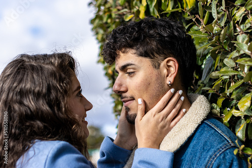 A young couple standing looking at each other with a wall of green leaves behind him
