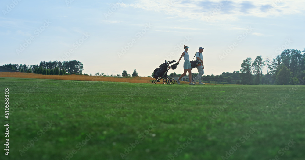 Golf players walk field on course. Golfing couple hold equipment clubs outside. Golf players walk field on course. Golfing couple hold equipment clubs outside.