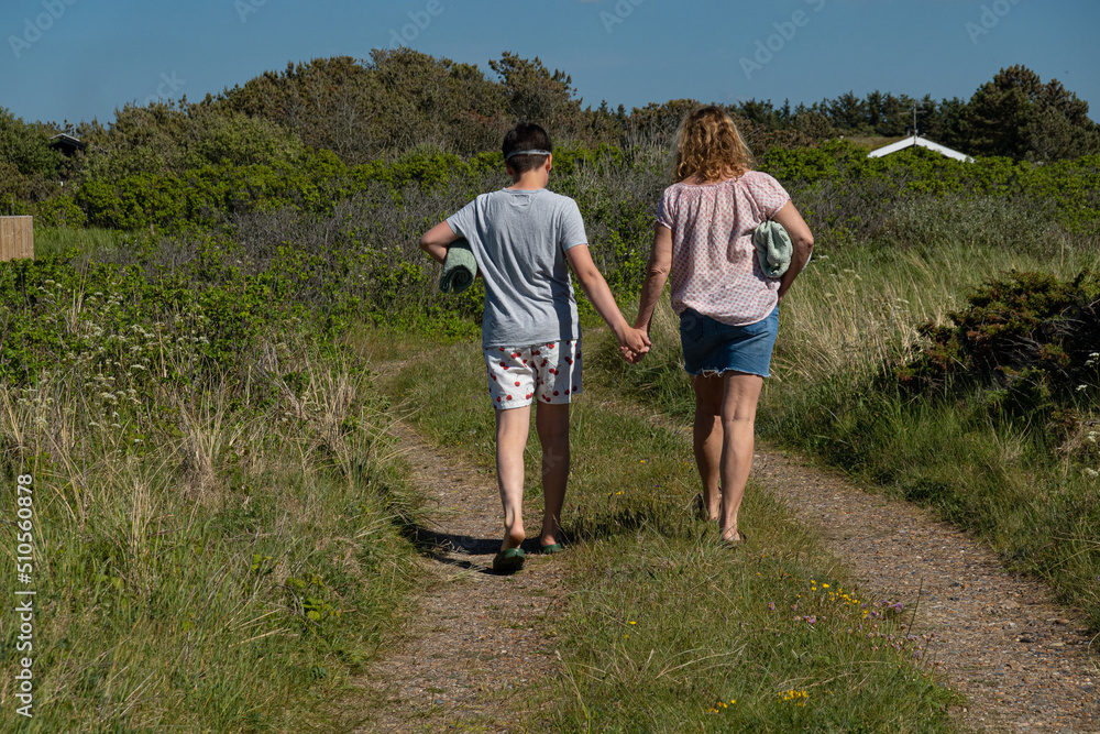 Hirtshals, Denmark A mother and son walk hand in hand a dirt road to the beach with towels . Hirtshals, Denmark A mother and son walk hand in hand a dirt road to the beach with towels .