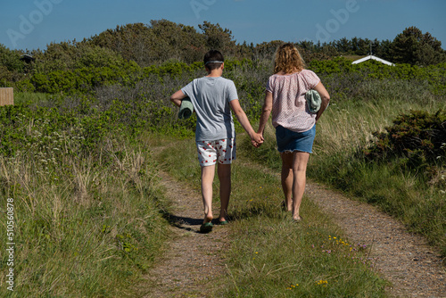 Hirtshals, Denmark A mother and son walk hand in hand a dirt road to the beach with towels .