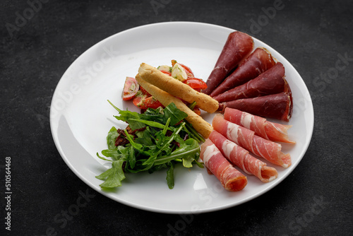 Meat appetizer with vegetable salad, arugula and grissini. Antipasti