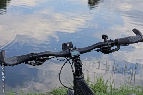 part of a sports bike with a black bicycle handlebar in green grass on the shore of a lake near gray water