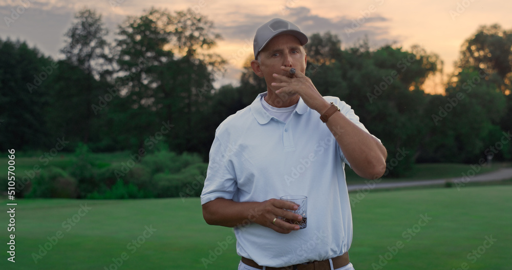 Rich golf player stand relaxed on course. Old man smoking cigar holding