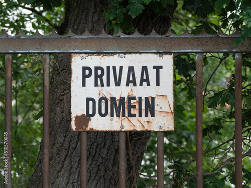white rusty plaque with black letters on an old fence that says Private domain in Dutch