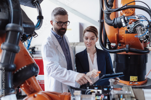 Robotics engineers with tablet dicussing and desinging modern robotic arm in factory. photo