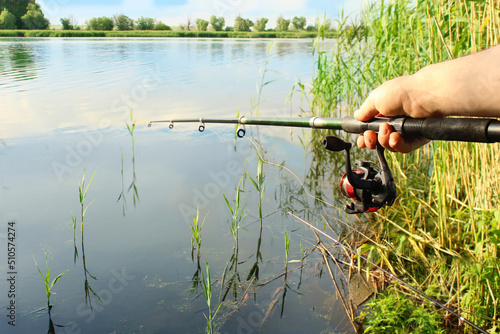 Close-up of the hands of a young fisherman holding a fishing rod on the shore of a lake on a summer sunny day outdoors. Catch carp, bream, crucian carp, perch, roach, perch, bleak, chebak. 