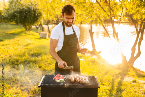 Male chef with wine checking meat and vegetables on grill