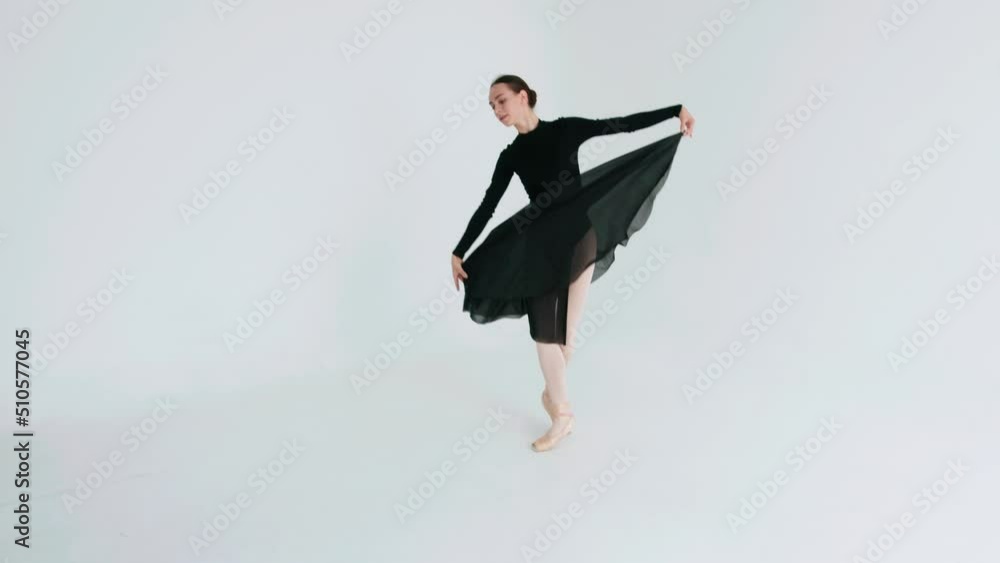 Ballerina in a black airy dress spins on her fingertips and becomes a releve pose while performing a classical dance in a white studio Ballerina in a black airy dress spins on her fingertips and becomes a releve pose while performing a classical dance in a white studio