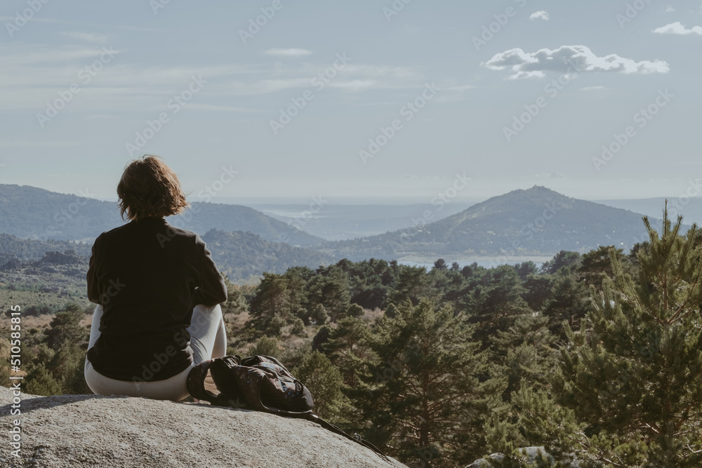 Young girl on the mountain, resting on a rock, looking at the landscape on the horizon, in the Mountain Range, Madrid, Spain.
