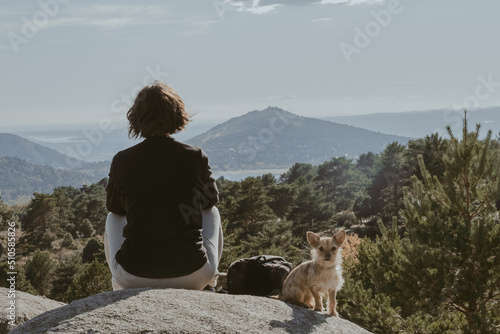 Young girl and her dog on a rock in the mountains, resting and looking at the scenery, in the Mountain Range of Madrid. photo