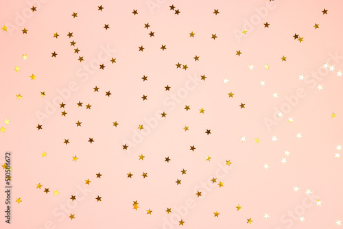 Golden star shaped glitter confetti on pink background. Festive flat lay holiday pastel backdrop.