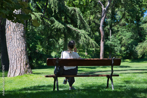Woman sitting on a park bench, talking on her mobile phone on a sunny day.