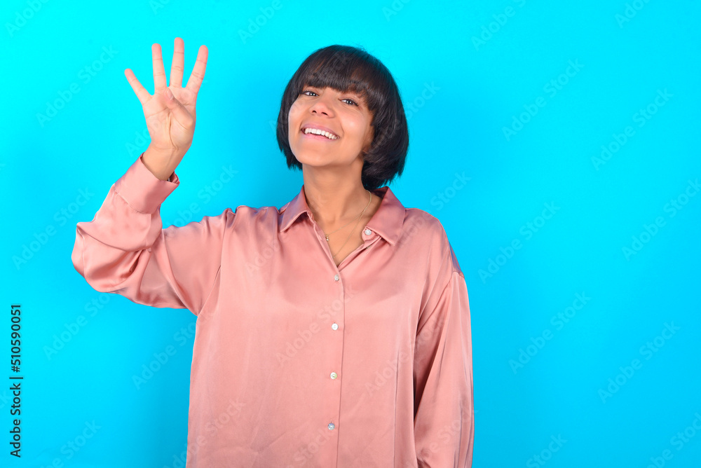 young brunette woman wearing pink silk shirt over blue background showing and pointing up with fingers number four while smiling confident and happy. young brunette woman wearing pink silk shirt over blue background showing and pointing up with fingers number four while smiling confident and happy.