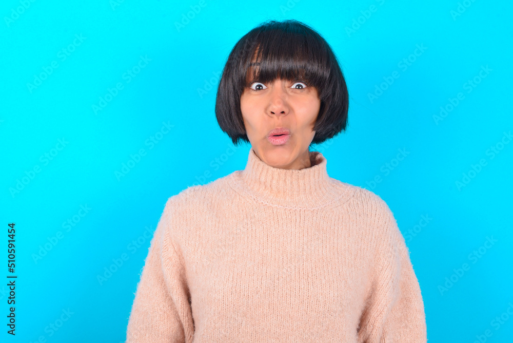 young brunette woman wearing pink knitted sweater over blue background expressing disgust, unwillingness, disregard having tensive look frowning face, looking indignant with something. young brunette woman wearing pink knitted sweater over blue background expressing disgust, unwillingness, disregard having tensive look frowning face, looking indignant with something.