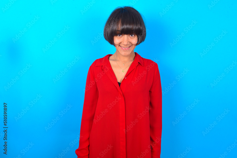 Fototapeta premium young brunette woman with short hair wearing red shirt over blue background with nice beaming smile pleased expression. Positive emotions concept