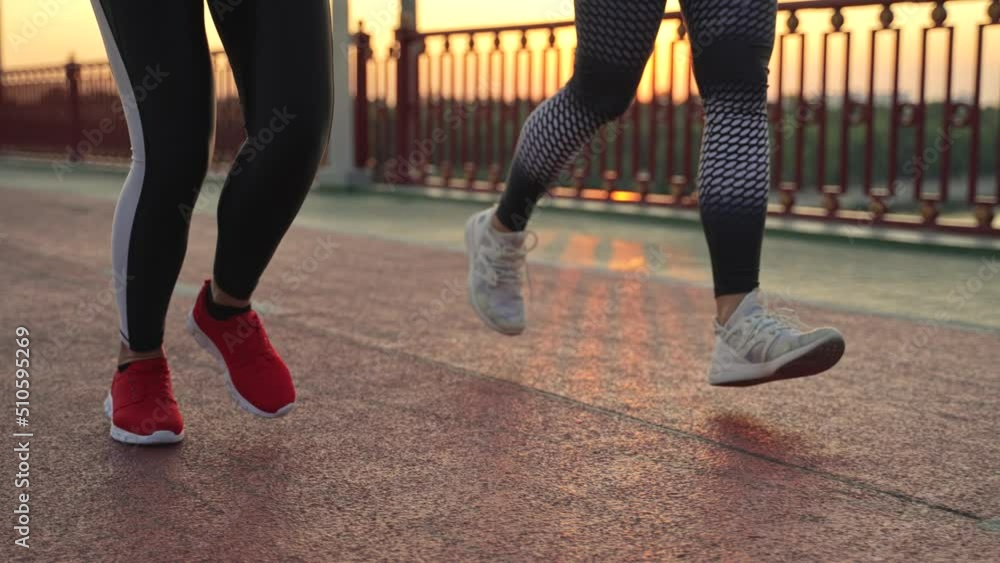 Close-up of female feet in sneakers running across footbridge during evening cardio workout. Two fit women in sportswear doing sports outdoors, active healthy hobby, uban activity concept Close-up of female feet in sneakers running across footbridge during evening cardio workout. Two fit women in sportswear doing sports outdoors, active healthy hobby, uban activity concept