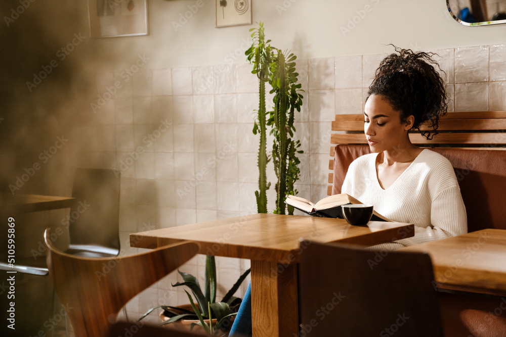 Young black woman drinking coffee and reading book in cafe Young black woman drinking coffee and reading book in cafe