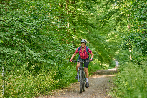 nice active senior woman riding her electric mountain bike in the green city forest of Stuttgart, Germany © Uwe