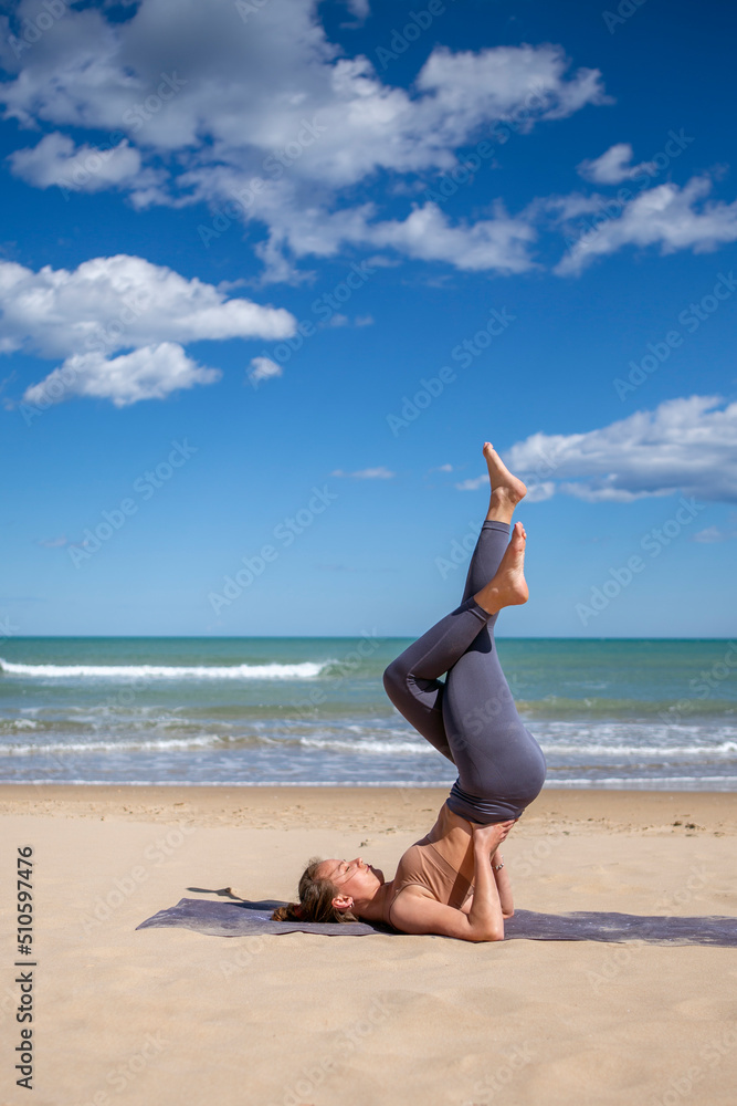 young woman doing pilates on the shore of the beach in sportswear