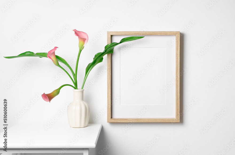 Empty wooden portrait frame mockup with calla flowers on white wall Empty wooden portrait frame mockup with calla flowers on white wall