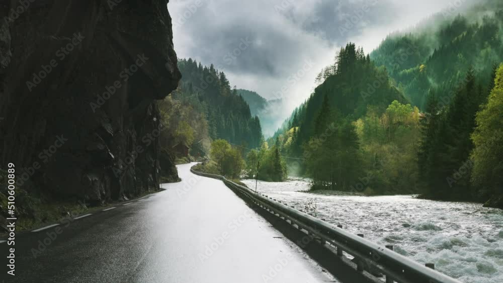 Revealing shot of the famous Latefossen waterfall, Norway. Water dust from the powerful torrent fills the air. Dense forest covers the mountain slopes. Slow-motion, pan forward.