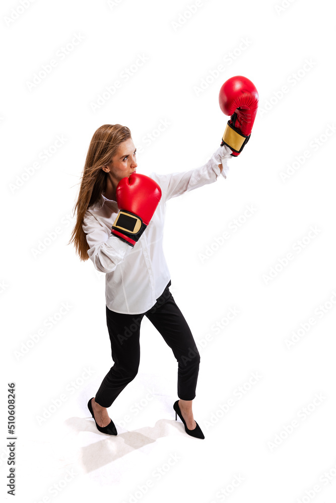 Full-length portrait of young woman, employee in office cloth and boxing gloves isolated over white studio background. Showing professional ambitions Full-length portrait of young woman, employee in office cloth and boxing gloves isolated over white studio background. Showing professional ambitions
