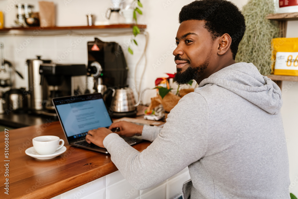 Black bearded man typing on laptop while working in cafe