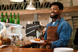 Black bearded man wearing apron laughing while working in cafe
