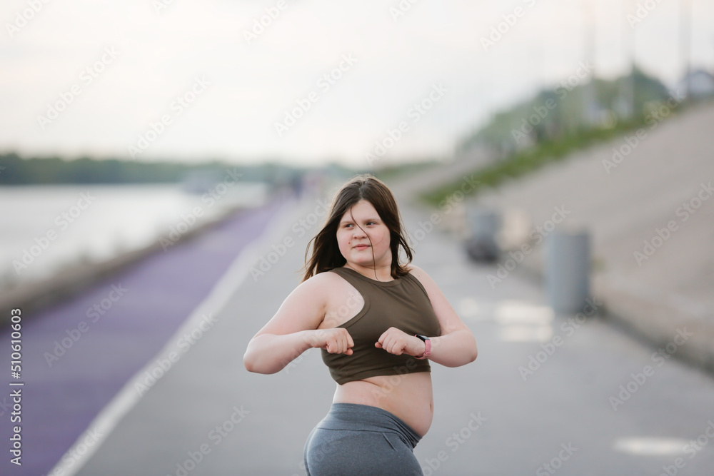 girl child teenager in sportswear with excess weight does exercises, plays sports outside in summer.