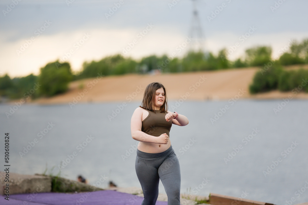 European teenage girl overweight on jog on treadmill along embankment of city, overweight and active lifestyle of teenager