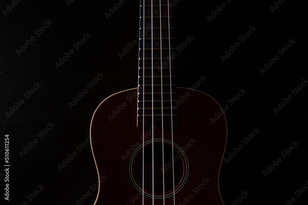 Ukulele brown wood grain in dark light for playing on black background.