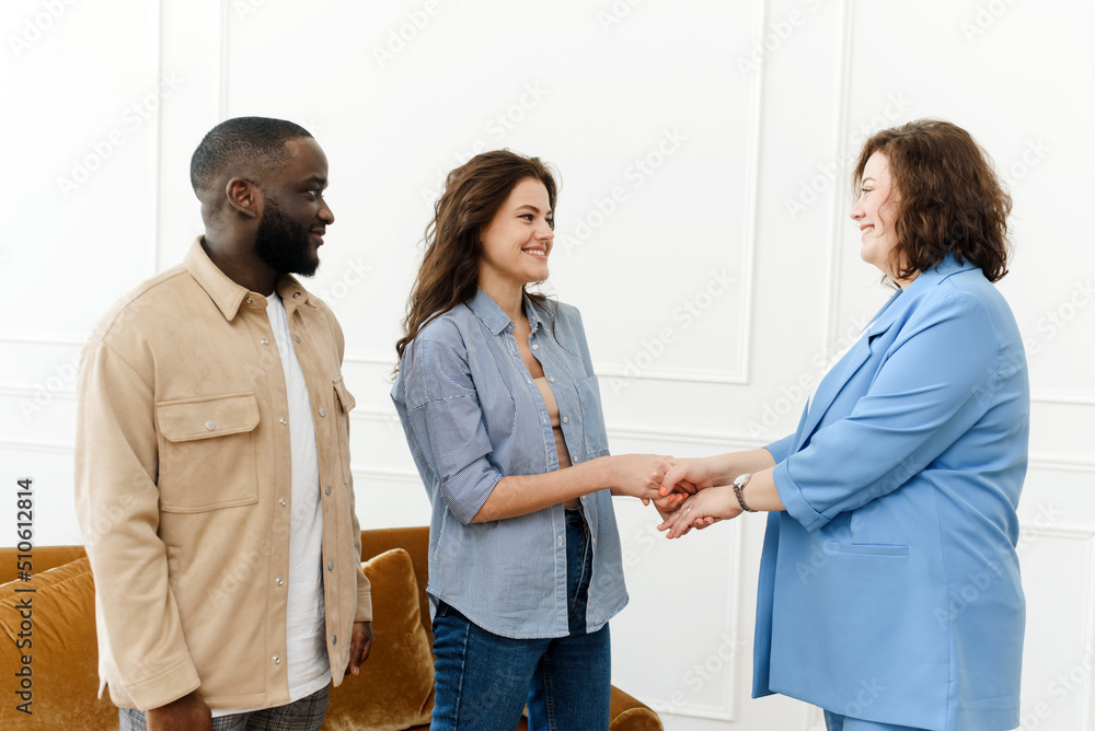 Fototapeta premium Female family psychologist shakes hands with a young woman. Young Diverse Couple Thanks Psychologist for Successful Session and Saved Marriage.