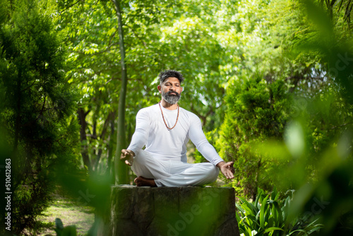 Indian man doing yoga meditation exercise in the green forest nature. fitness and healthy lifestyle.