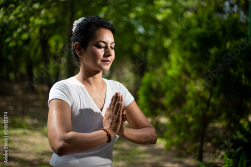 Beautiful indian woman doing yoga exercise while sitting in the green forest nature, Asian female meditation pose, closeup