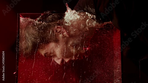 Portrait of a man immersing his face in water. Dark video with red light. Man screaming emotion underwater
