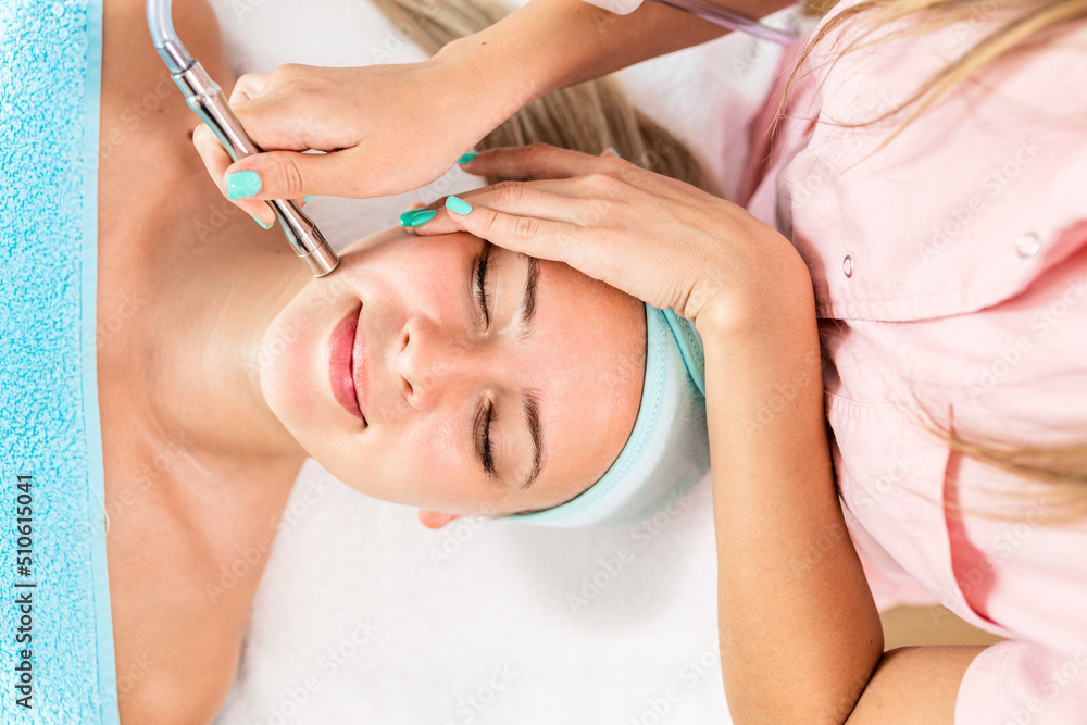 Naklejka premium Beautician therapist applying face treatment in beauty salon to young woman.