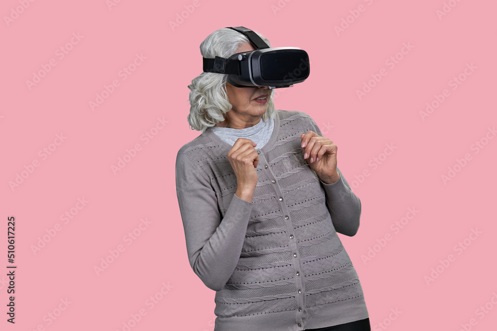 Frightened senior woman using virtual glasses standing on color background. People and modern technology concept. Frightened senior woman using virtual glasses standing on color background. People and modern technology concept.