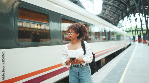 Close-up portrait of a young woman in glasses with a smartphone and backpack stands at the station. Positive woman using mobile phone outdoors in urban background.