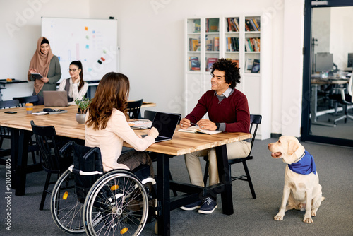 Happy black businessman communicating with female colleague with disability while working together at pet friendly office. photo
