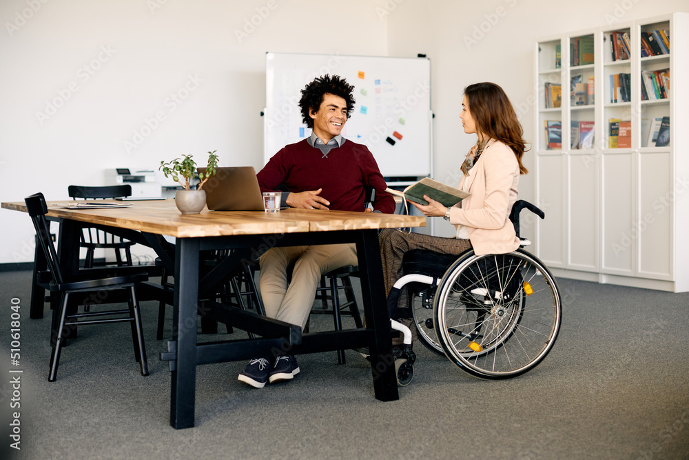Happy black businessman talks to female colleague with disability in office. Happy black businessman talks to female colleague with disability in office.
