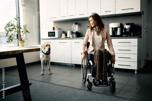 Happy businesswoman in wheelchair and her assistance dog at office kitchen.