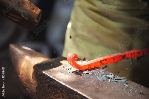 Fotografija Professional male blacksmith forming red hot metal on an anvil in interior blacksmith workshop