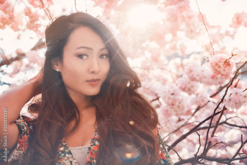Young Asian woman, in a floral pattern dress, in front of blossoming cherry tree in the spring time Young Asian woman, in a floral pattern dress, in front of blossoming cherry tree in the spring time