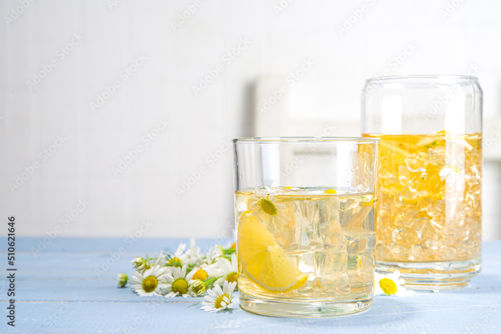 Herbal organic cold drink. Infused flower water. Iced daisy Chamomile tea or lemonade with lemon slice and ice cubes, in two different glasses, blue wooden background copy space Herbal organic cold drink. Infused flower water. Iced daisy Chamomile tea or lemonade with lemon slice and ice cubes, in two different glasses, blue wooden background copy space